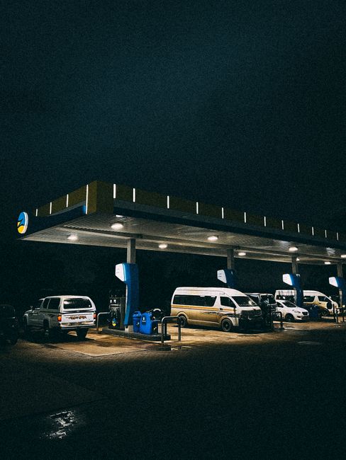 A nighttime view of a garage-style parking area connected to Upton Park Station in West Ham, featuring a large flat-roofed canopy with built-in lighting illuminating the space below. Under the canopy,