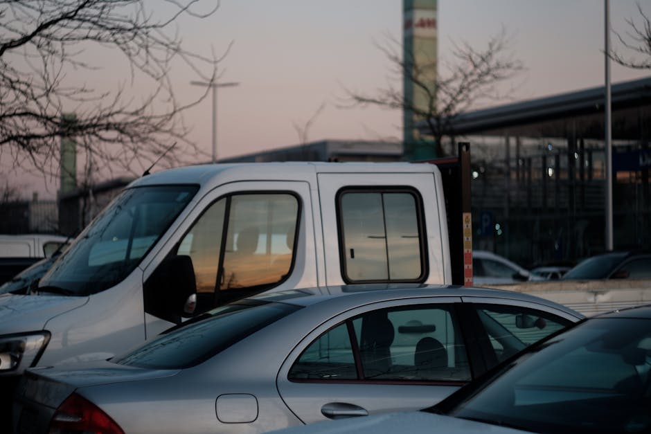 A nighttime view of a garage-style parking area connected to Upton Park Station in West Ham, featuring a large flat-roofed canopy with built-in lighting illuminating the space below. Under the canopy,